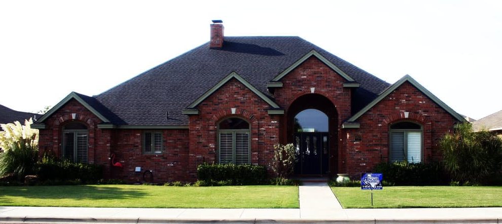 After: brick home in Lubbock with a new dark shingle roof and a Kincaid yard sign