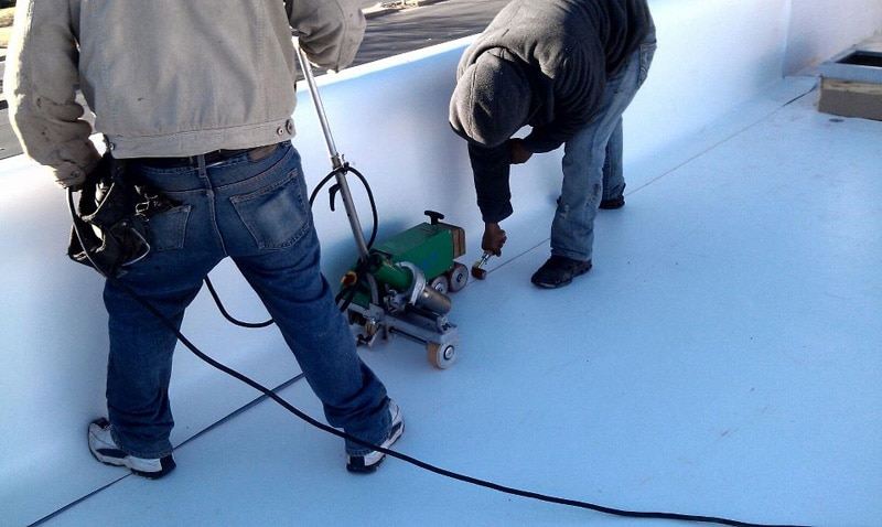 Roofer heat-welding a white flat roof on a commercial building
